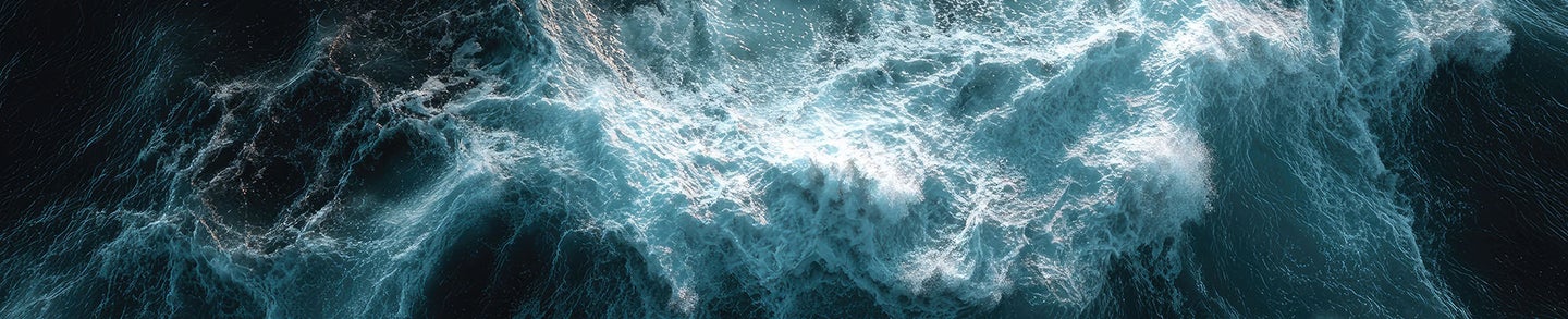 A close-up, abstract view of turbulent ocean waves with swirling patterns of turquoise and white foam against a dark, deep blue background.