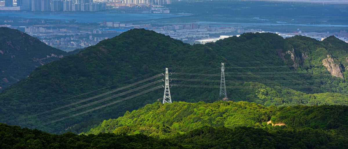 High voltage transmission lines are erected on the top of the mountain, and the city in the background