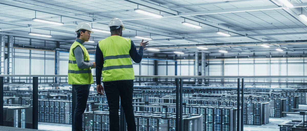 Korean Data Center System Administrators and African American IT Specialists in High Visibility Vests Talk, Use Laptop. IT Engineers work on Cyber Security Network Protection in Server Farm.