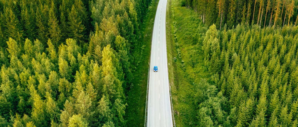 Aerial view from above of country road through the green summer forest in summer Finland. drone photography