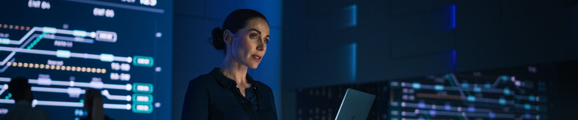 Beautiful Confident Female Project Manager works on Laptop Standing in Telecommunications System Control Room. In Background Big Screen Showing Infographics of Infrastructure, Charts, System Analysis