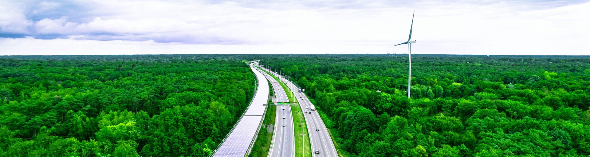 Aerial view taken with drone flying above multiple lane highway crossing luxuriant infinite forest with plain horizon, next to, the Peerdsbos railway tunnel covered with solar pannels with kilometers long. Antwerp. Belgium
