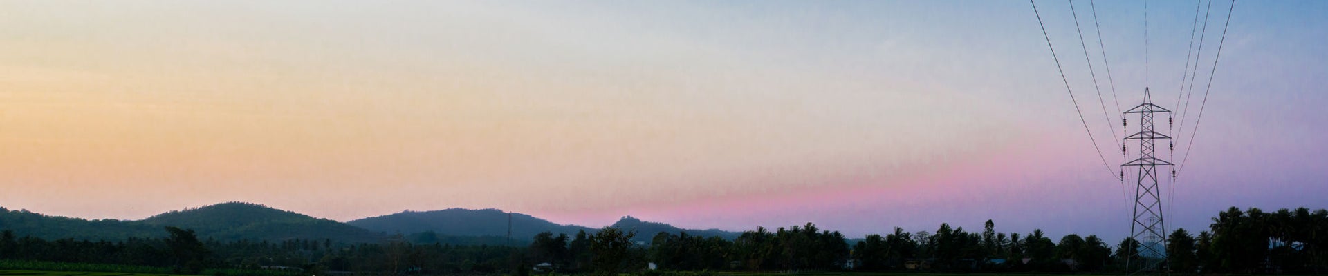 Power grid and power lines in green paddy fields in rural India. Mountain ranges seen at a distance. Colorful evening sky. Copy space for adding text.