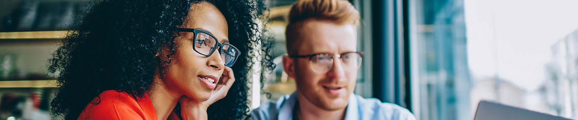 Dark skinned female graphic designer pointing with finger on laptop computer during collaboration with caucasian colleague on common project in coffee shop.Two multicultural friends discussing website