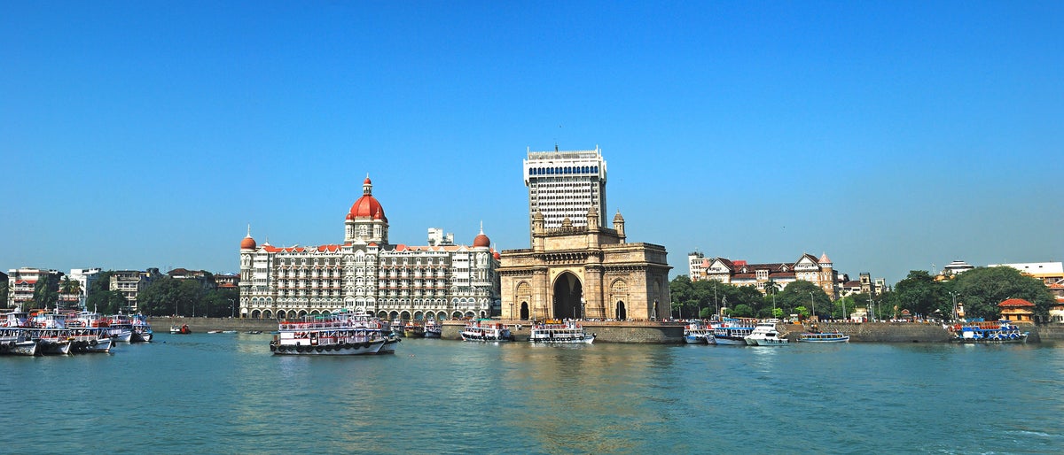 Wide angle panoramic view of Mumbai's famous heritage landmark Gateway of India as seen from the Arabian sea and busy sea front with colorful excursion ferry boats in foreground. Copy space.