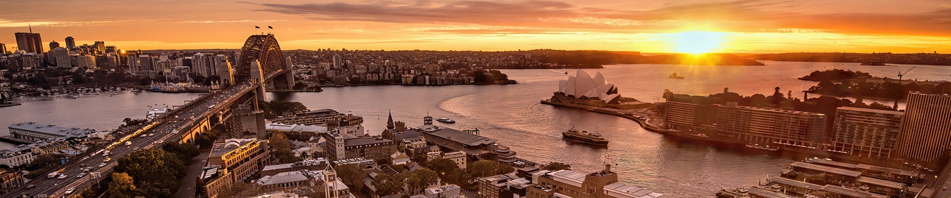 The sun rises over Sydney Harbour in Sydney, Australia. The harbor features two famous landmarks - the Sydney Opera House and Sydney Harbour Bridge.