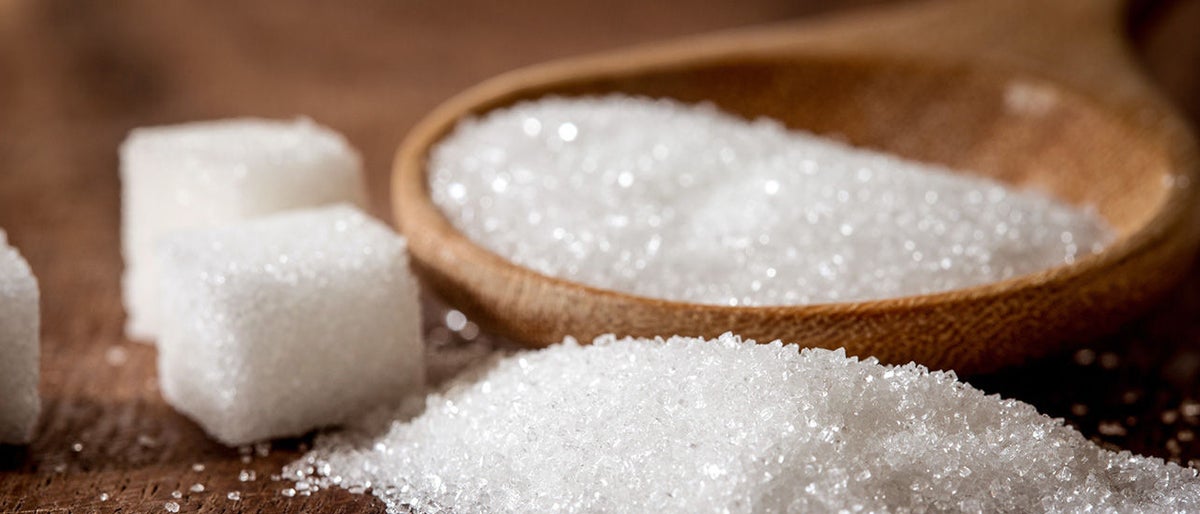 Close up sugar cubes and cane in wooden spoon on the table 
