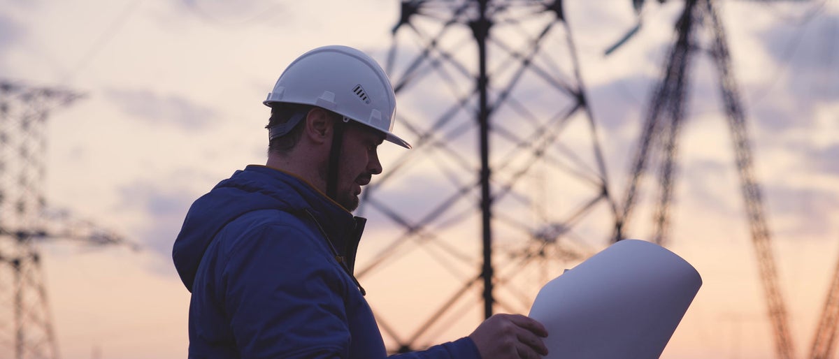 An electrician on the background of high towers of power plants looks at the project for the development of an electrical structure, the expansion of the electrical voltage of volts in the wires