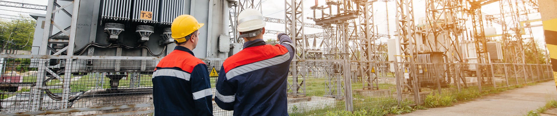Two specialist electrical substation engineers inspect modern high-voltage equipment during sunset. Energy. Industry