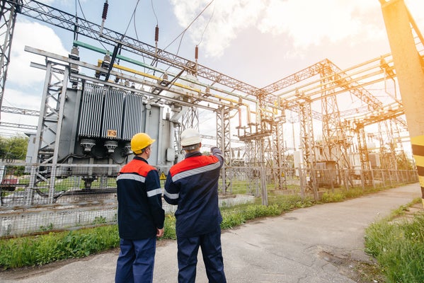 Two specialist electrical substation engineers inspect modern high-voltage equipment during sunset. Energy. Industry