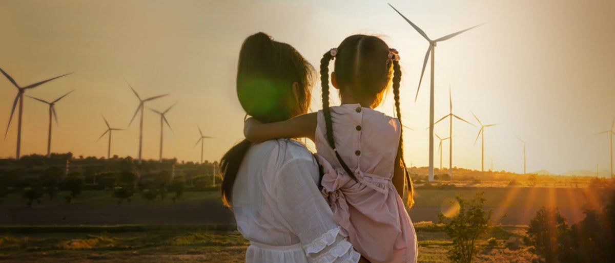 woman carrying a child looking at windmills for sustainable future