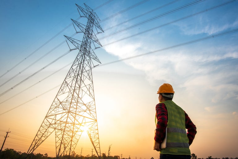 Picture of an electrical engineer standing and watching at the electric power station to view the planning work by producing electricity at high voltage electricity poles.