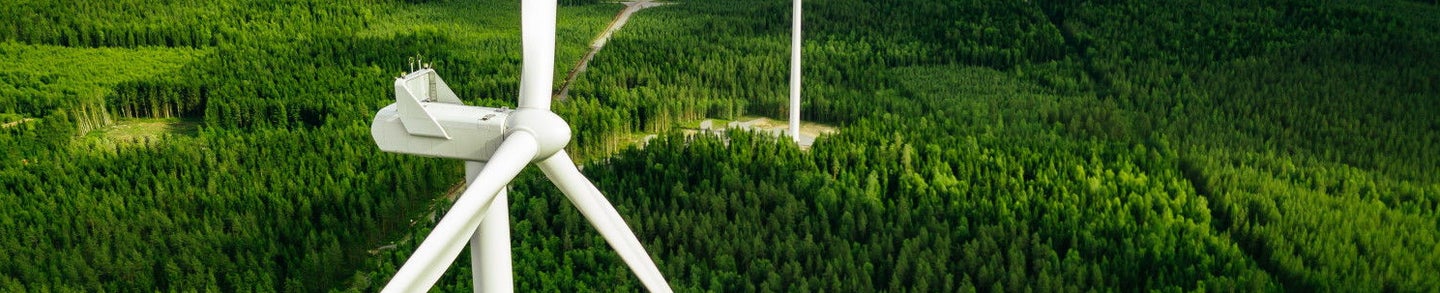 Aerial view of windmills in green summer forest in Finland. Wind turbines for electric power with clean and Renewable Energy
