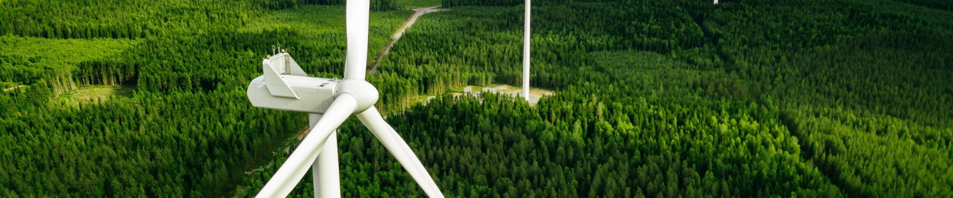Aerial view of windmills in green summer forest in Finland. Wind turbines for electric power with clean and Renewable Energy