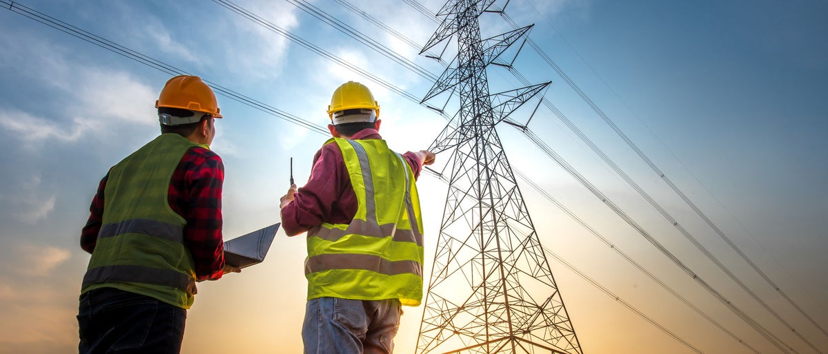 Picture of two electrical engineers using a notebook computer standing at a power station to view the planning work by producing electrical energy at high voltage electrodes.