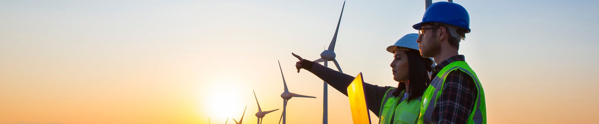 Young maintenance engineer team working in wind turbine farm at sunset